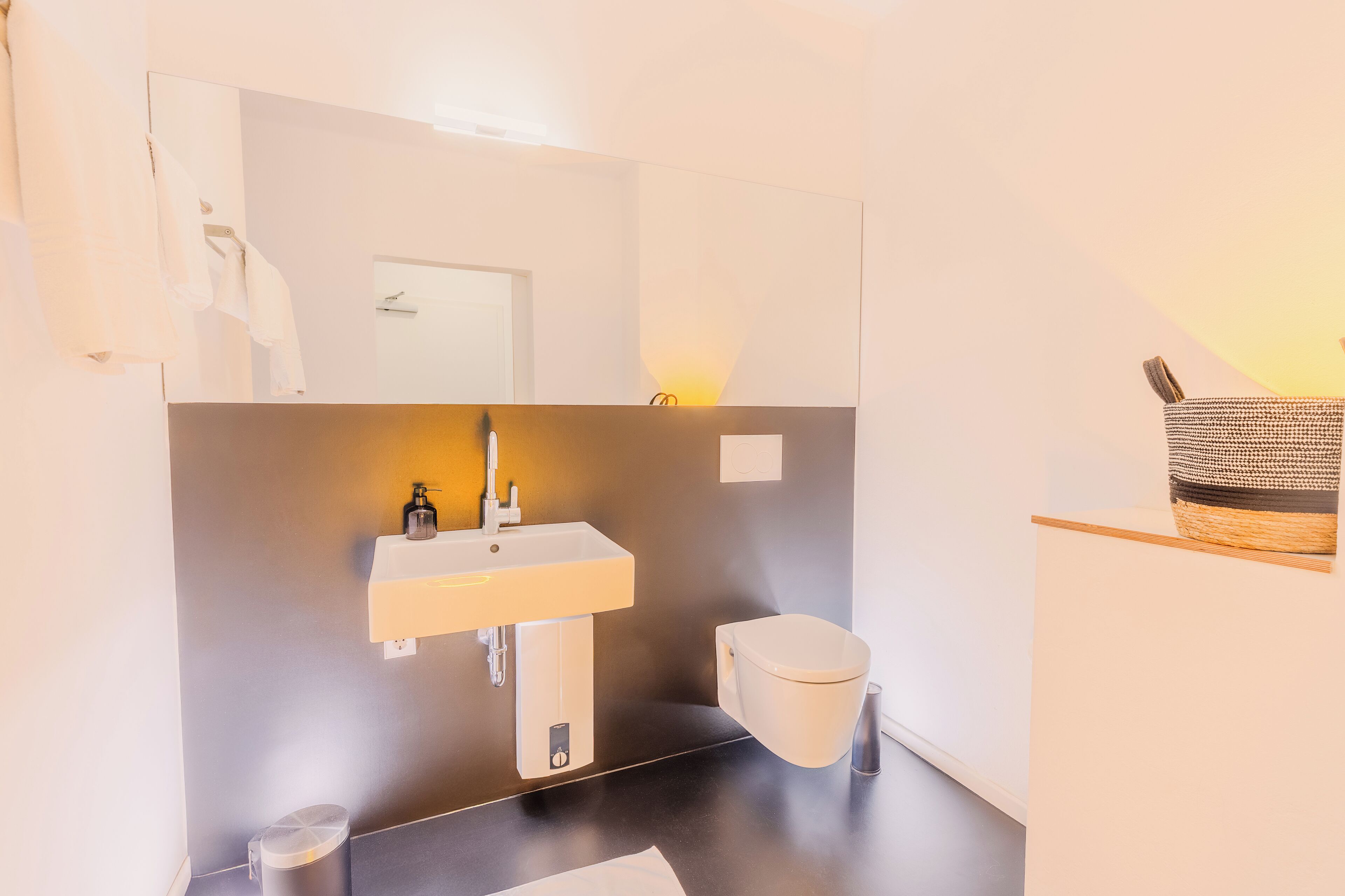 A modern bathroom with a white sink, mirror, and toilet.