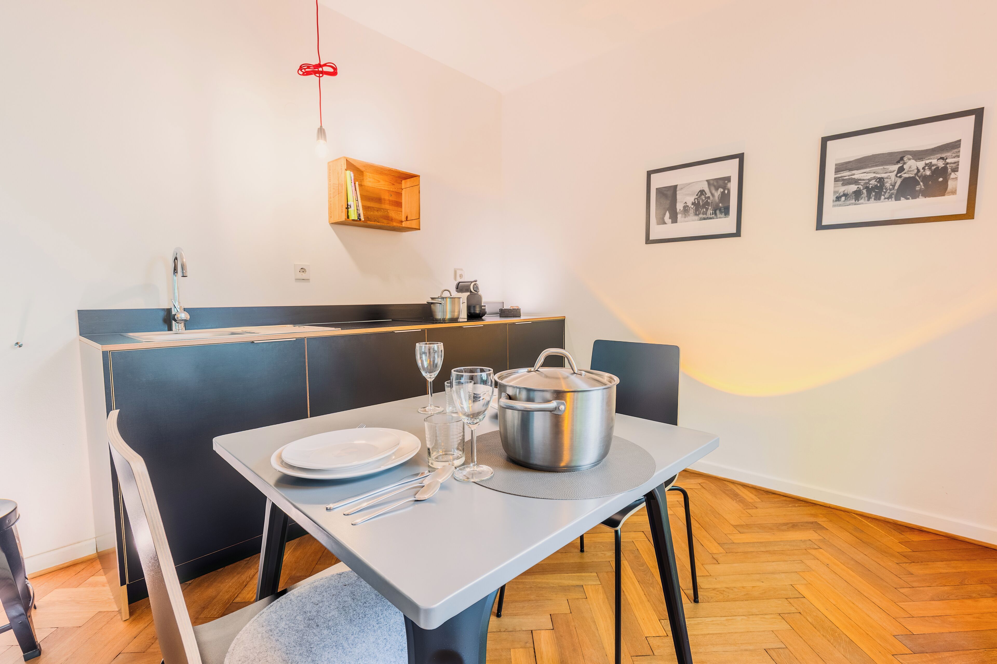 A compact kitchen with a dining area, a wooden shelf, and two framed pictures on the wall.