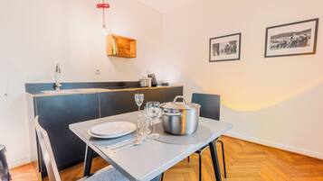 A compact kitchen with a dining area, a wooden shelf, and two framed pictures on the wall.