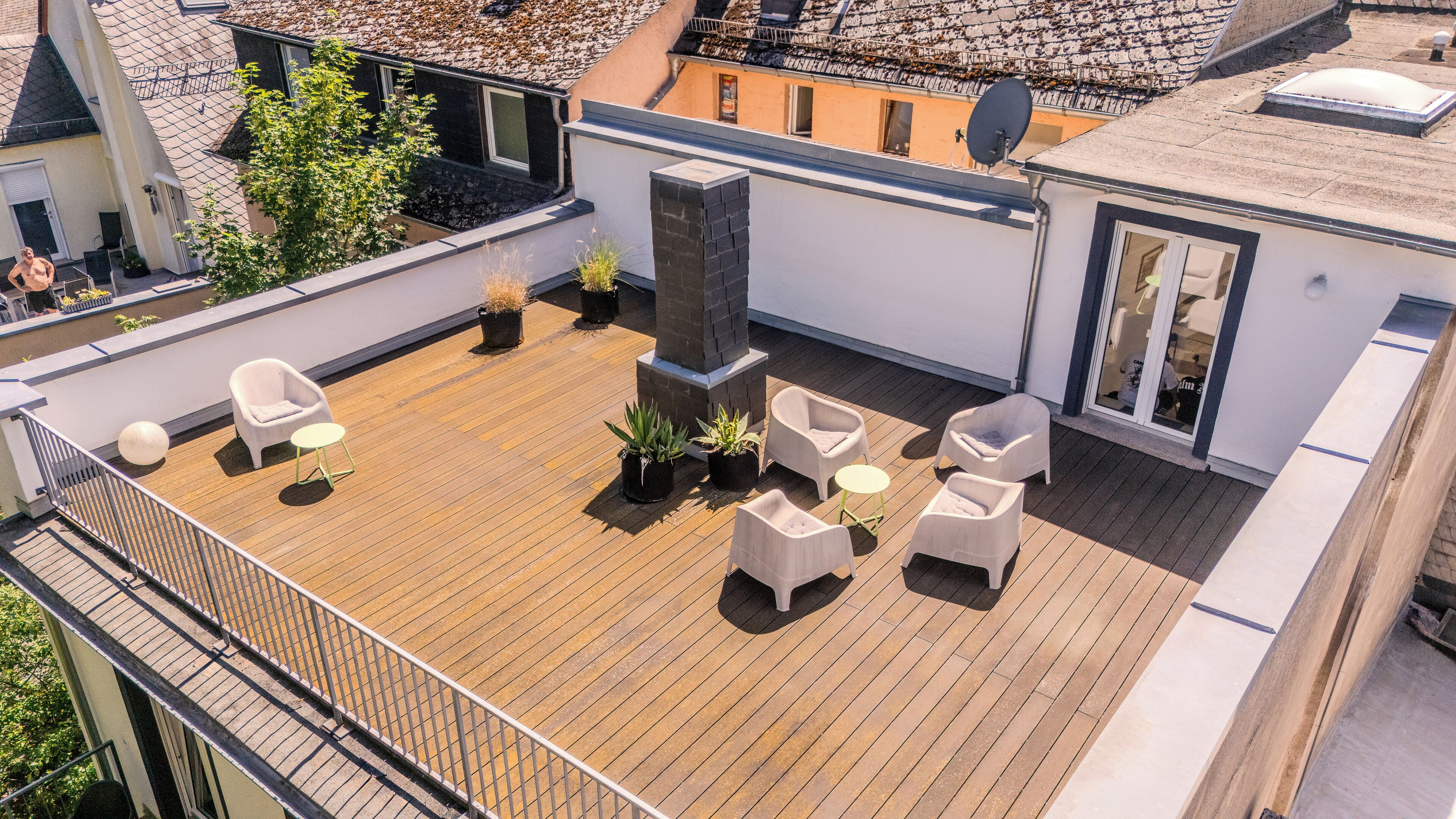 Une terrasse sur le toit avec un plancher en bois, des meubles d’extérieur blancs et des plantes en pot.