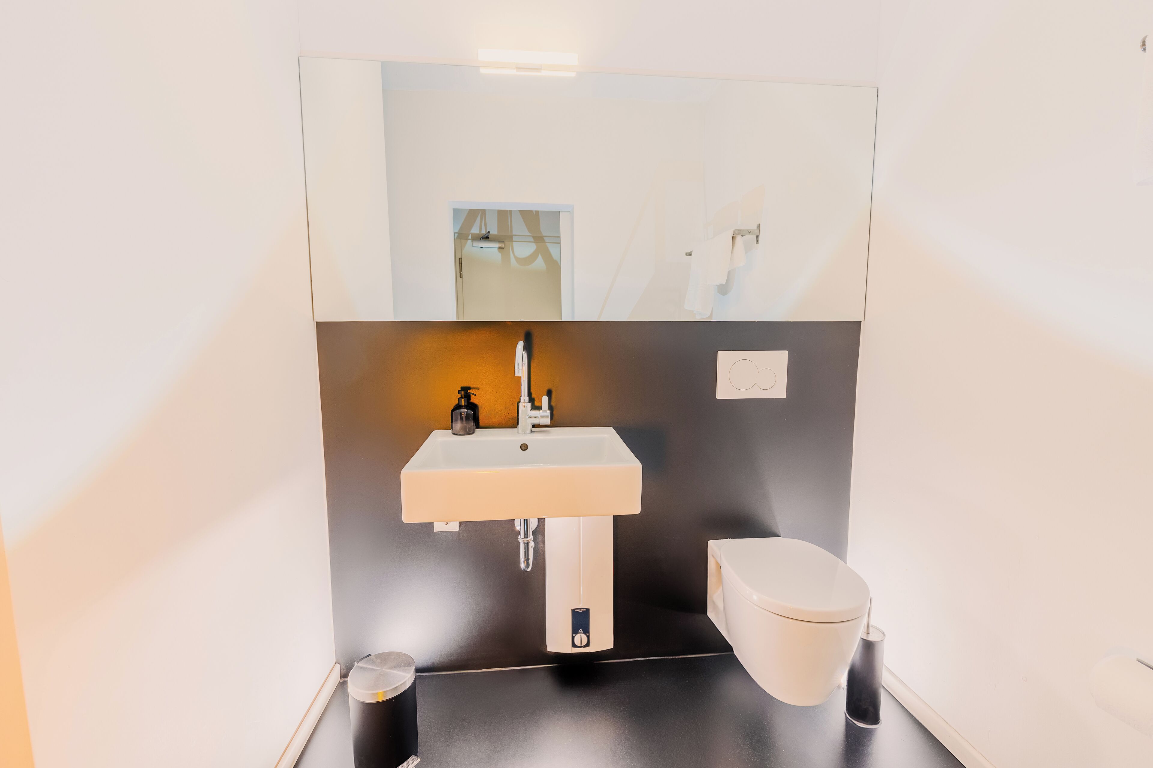 Un baño moderno con un lavabo blanco, un inodoro y un espejo sobre el lavabo.
