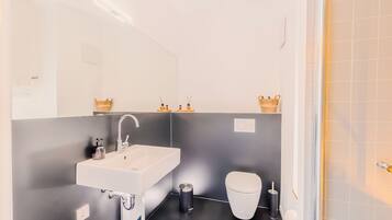 A modern bathroom with a white sink, a toilet, and a mirror. There are baskets on the wall and a trash can on the floor.