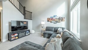 Un salon moderne avec un canapé gris, un téléviseur à écran plat, un escalier et des tableaux encadrés accrochés au mur.
