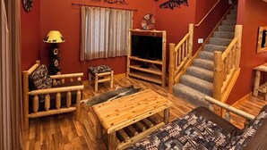A cozy living room with a wooden staircase, a flat-screen TV, and a clock on the wall.