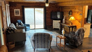 En mysig stuga med stengolv, träväggar, en tv och en öppen spis.