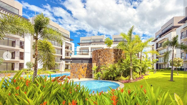 Un hotel moderno con piscina central rodeada de exuberante vegetación y palmeras.