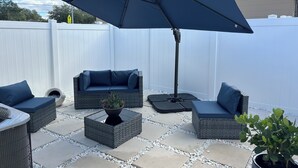 Une terrasse aménagée avec du mobilier d’extérieur, notamment un canapé et des fauteuils, une table avec une plante et un grand parasol.