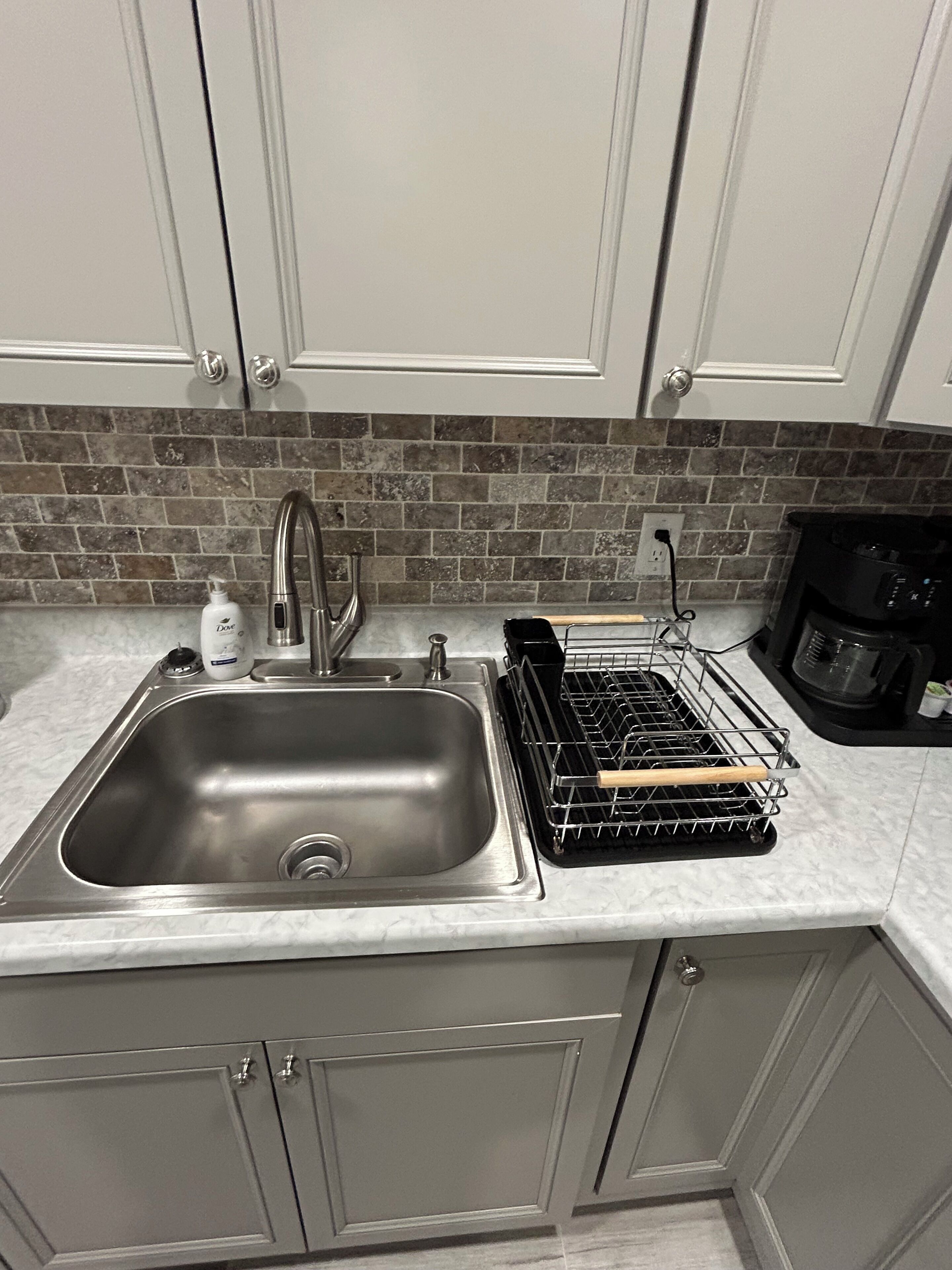 A kitchen with a stainless steel sink, a dish rack, and a coffee maker.