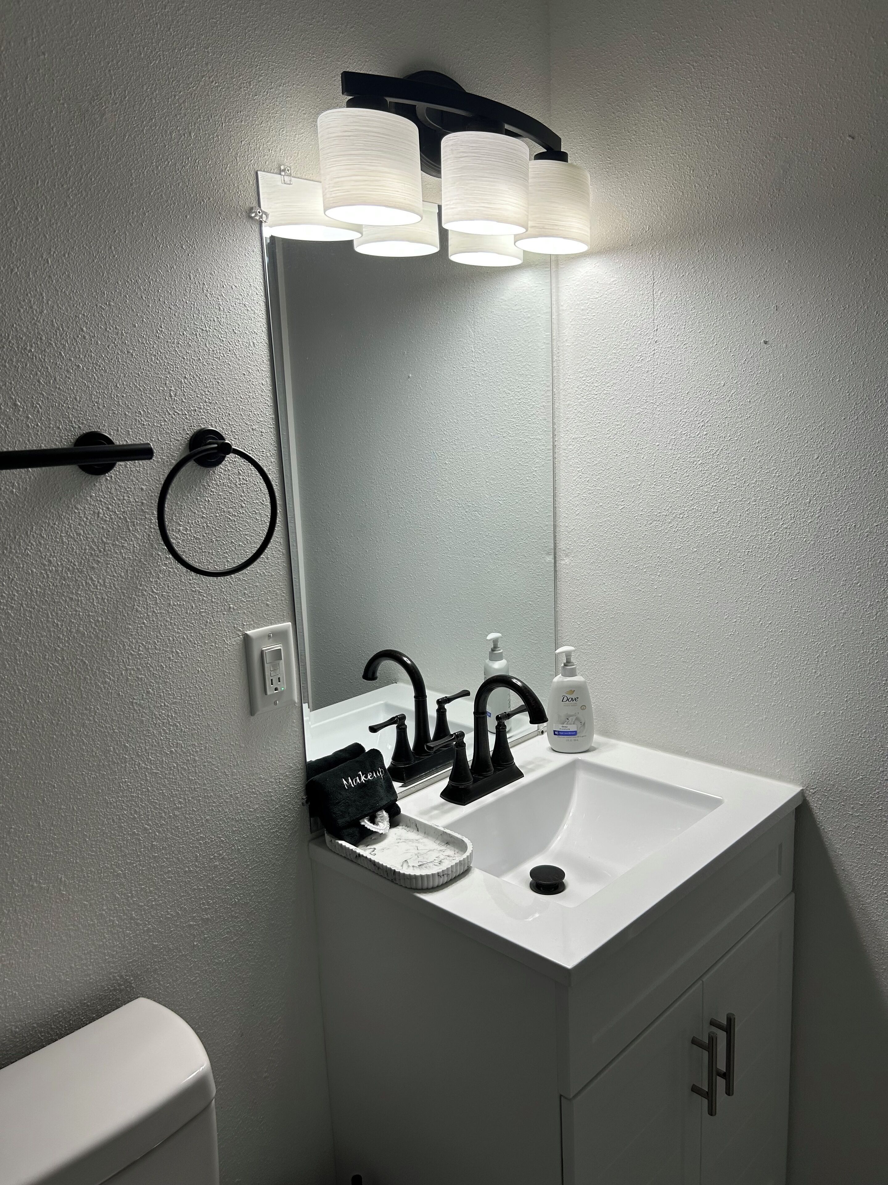 A bathroom with a white sink, black faucet, and a mirror with three lights above it.