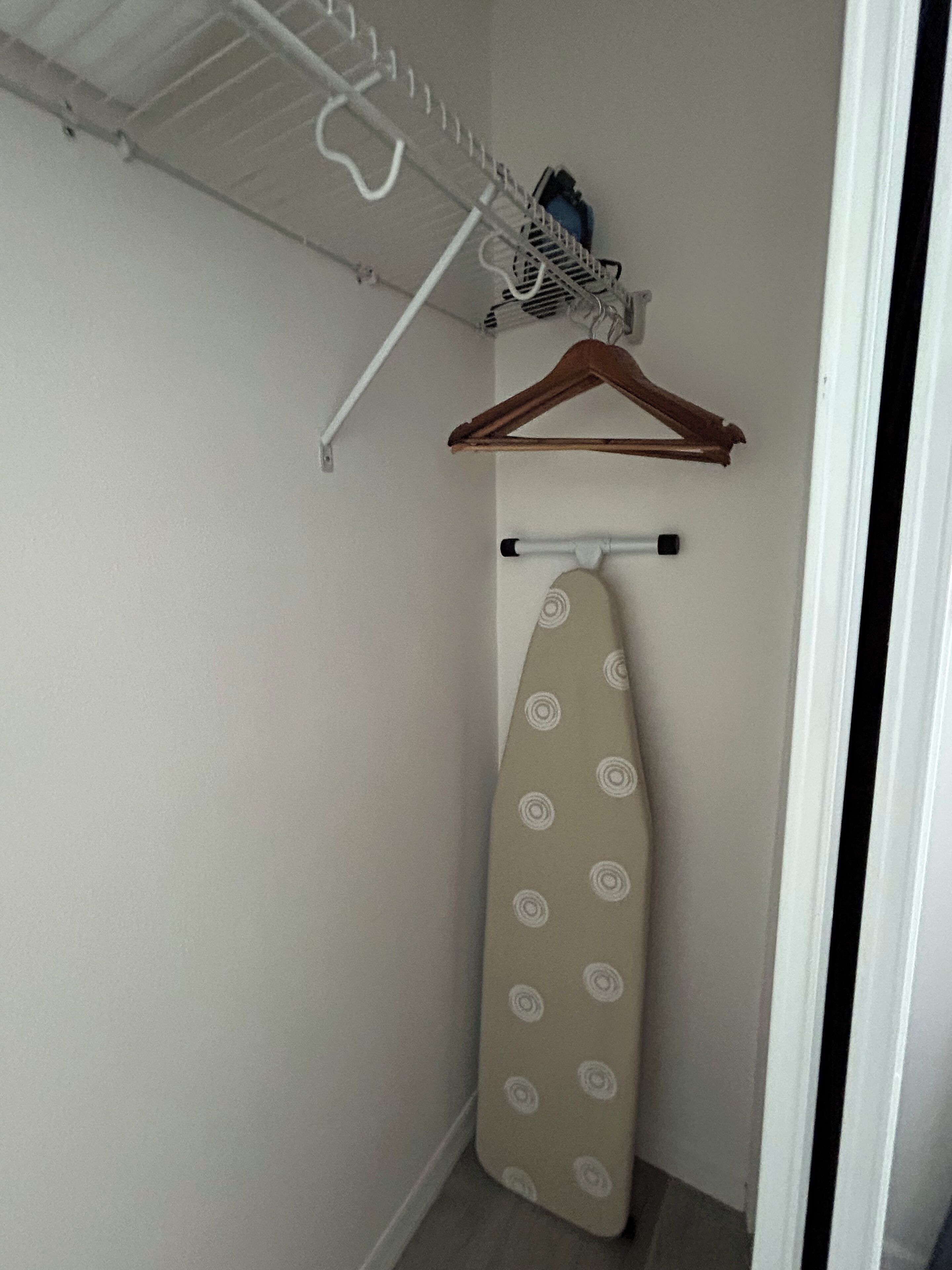 A small, enclosed space with a hanging rack, an ironing board, and a wooden hanger.