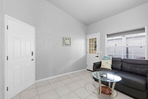 A living room with a glass coffee table, a leather sofa, and a door with a window. - Charming Pet-Friendly 2BR + Sleeper Sofa + Near Beach Drive (Port Orange)