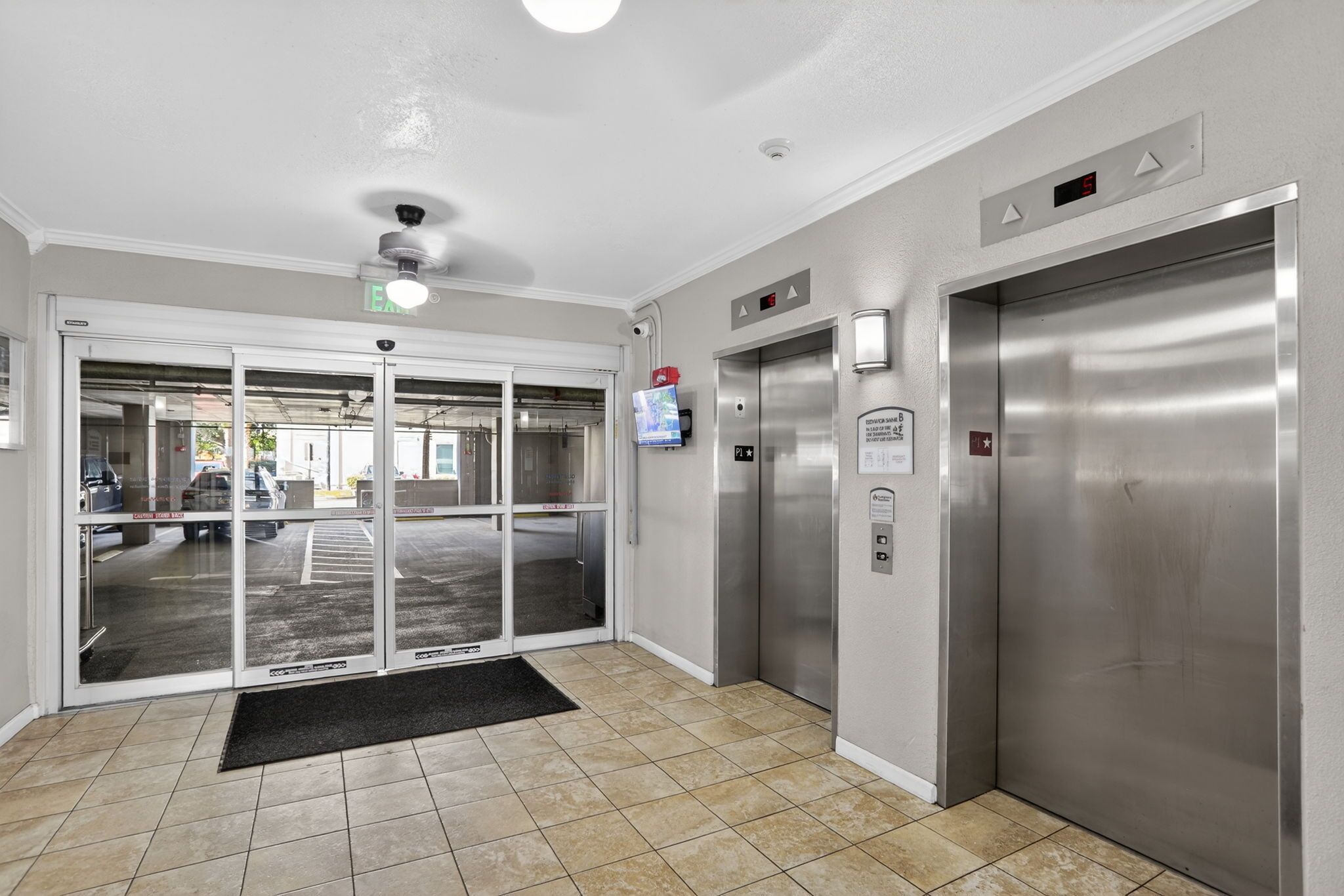 A modern elevator area with a digital display, a security camera, and a fire alarm.