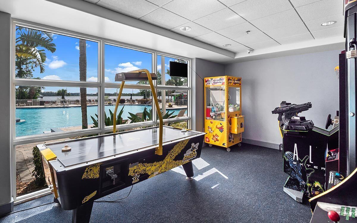 A pool table with a view of a pool outside, a claw machine, and a toy gun arcade.