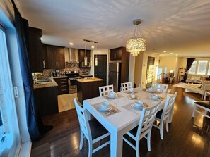 Een moderne keuken met donkerhouten kastjes, een centraal eiland en een eethoek met witte stoelen en een tafel voor vier personen.