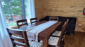 A wooden dining table with cushioned chairs, a woven table runner, and a view of the outdoors through a glass door. - Cabaña Aida Epuyén - comfortable and bright cabin in a natural setting (Epuyén)