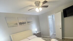 Una camera da letto con un letto, un comodino, una ventola a soffitto e una porta.