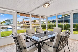A covered patio with a glass table and chairs, overlooking a canal with boats and houses. - Bay Breeze - Waterfront Retreat with Large Dock (Hernando Beach)