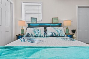 A bedroom with a bed, two nightstands, a window with blinds, and a door. - BRAND NEW REMOLDED Bay Breeze On The Coast (Hernando Beach)