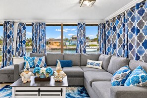 A modern living room with a grey sectional sofa, decorative pillows, a coffee table with a vase of flowers, and a 'NO WAKE ZONE' sign. - Bay Breeze - Waterfront Retreat with Large Dock (Hernando Beach)