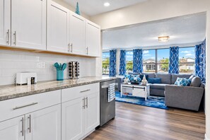 A modern kitchen with white cabinets, a marble countertop, and a built-in dishwasher. - Bay Breeze - Waterfront Retreat with Large Dock (Hernando Beach)