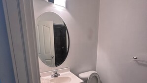 Et badeværelse med en hvid vask, et spejl, et toilet og en dør.