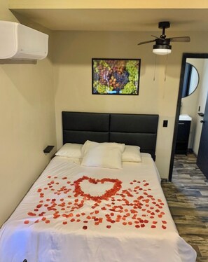 Ein Hotelzimmer mit einem Bett, einem Deckenventilator, einem gerahmten Bild an der Wand und einem Spiegel an der Tür.