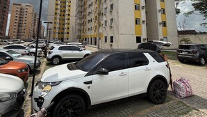 Ein Parkplatz mit mehreren Autos, einem weißen SUV und einem Roller.