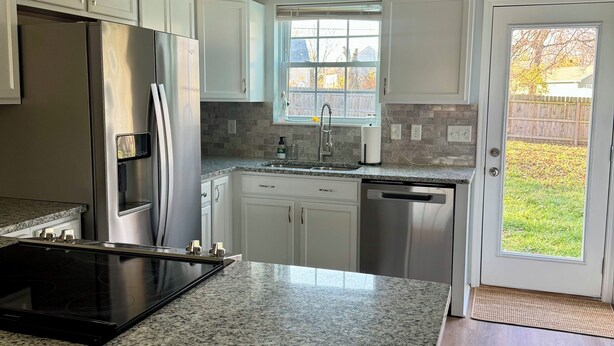 Una cocina moderna con encimeras de granito, electrodomésticos de acero inoxidable y armarios blancos.