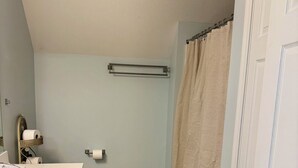 Un baño con inodoro, toallero, cortina de ducha y piso de madera.