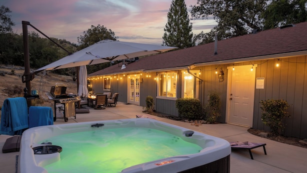 A hot tub in a backyard with a covered patio area, outdoor furniture, and string lights. - Moonrise Retreat, SPA, Near Yosemite & Bass Lake (Oakhurst)