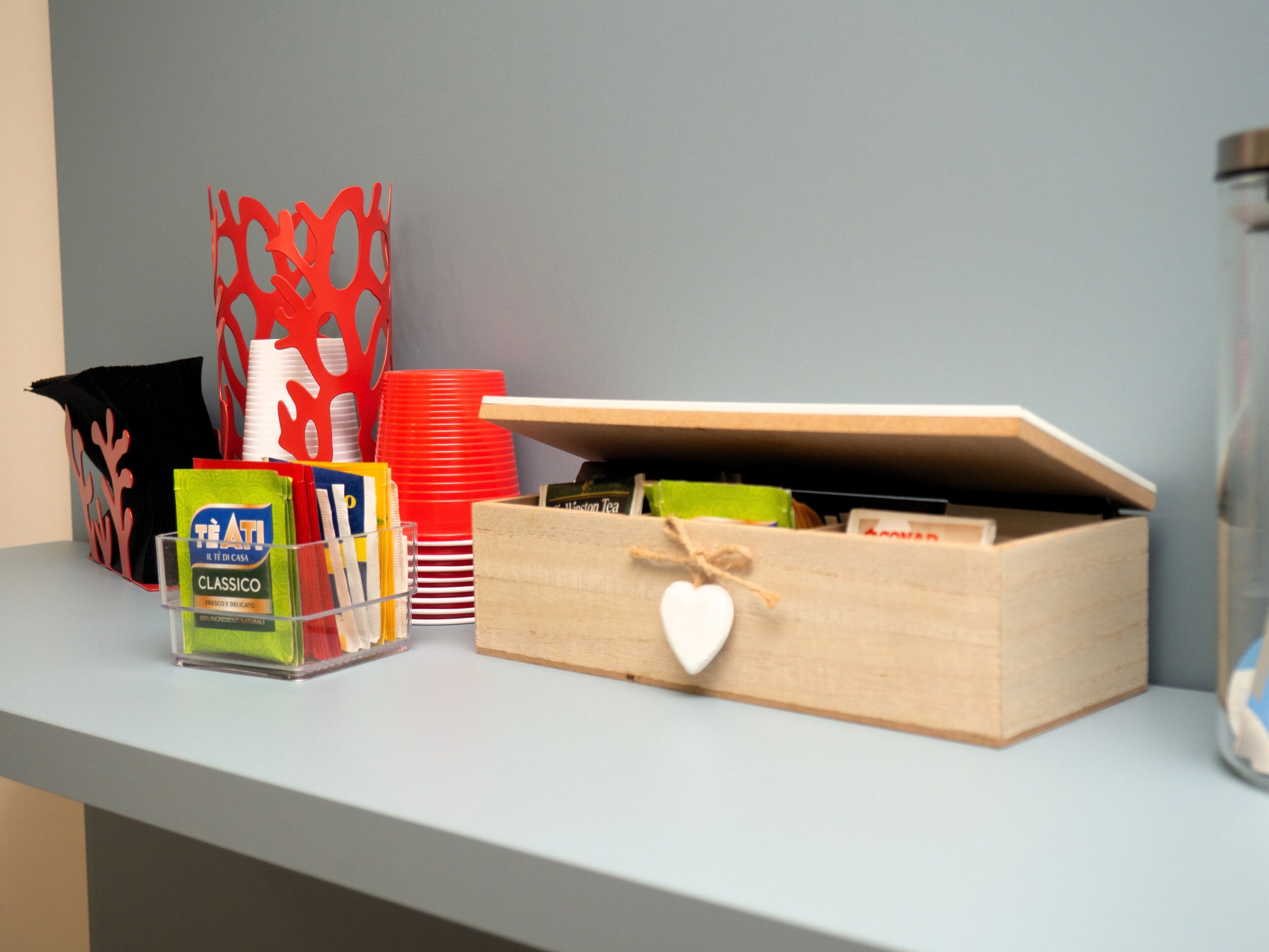 Una estantería con una caja de madera, vasos de plástico rojo y blanco, una bolsa verde y un adorno negro y rojo.