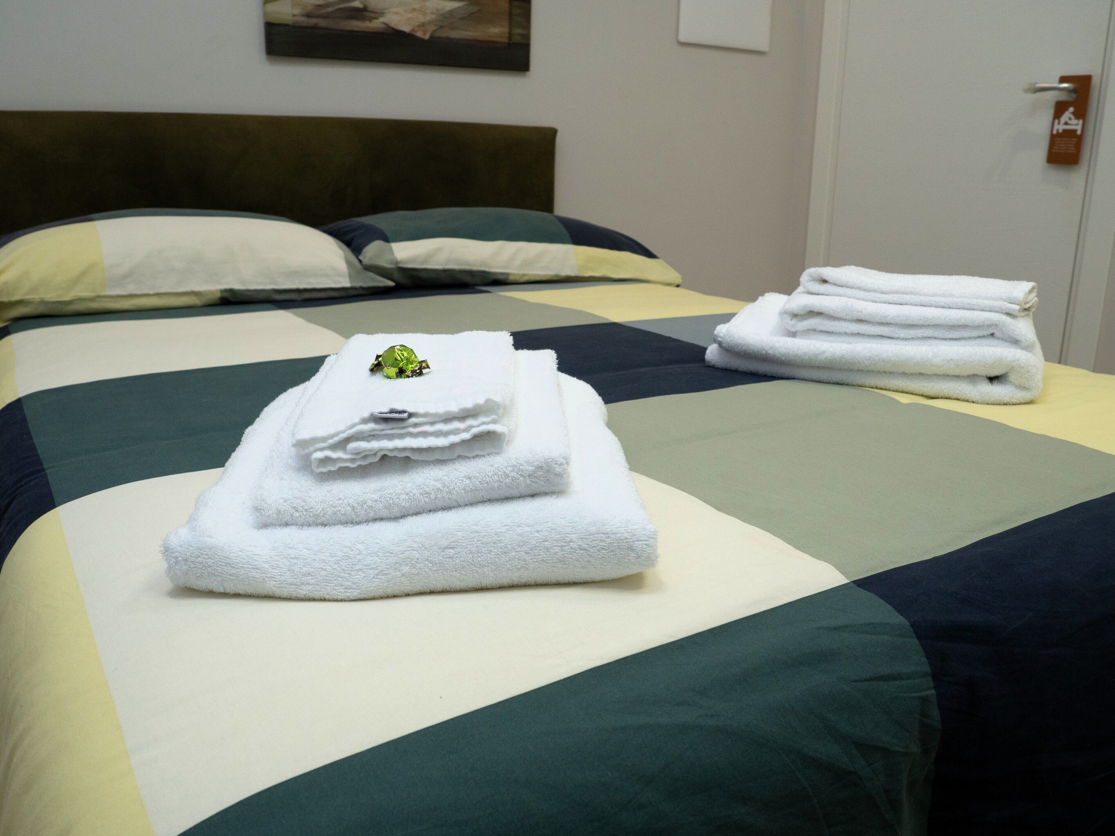 Una cama bien hecha con un cubrecolcha verde y blanco a rayas, una toalla blanca doblada encima y un pequeño objeto decorativo.