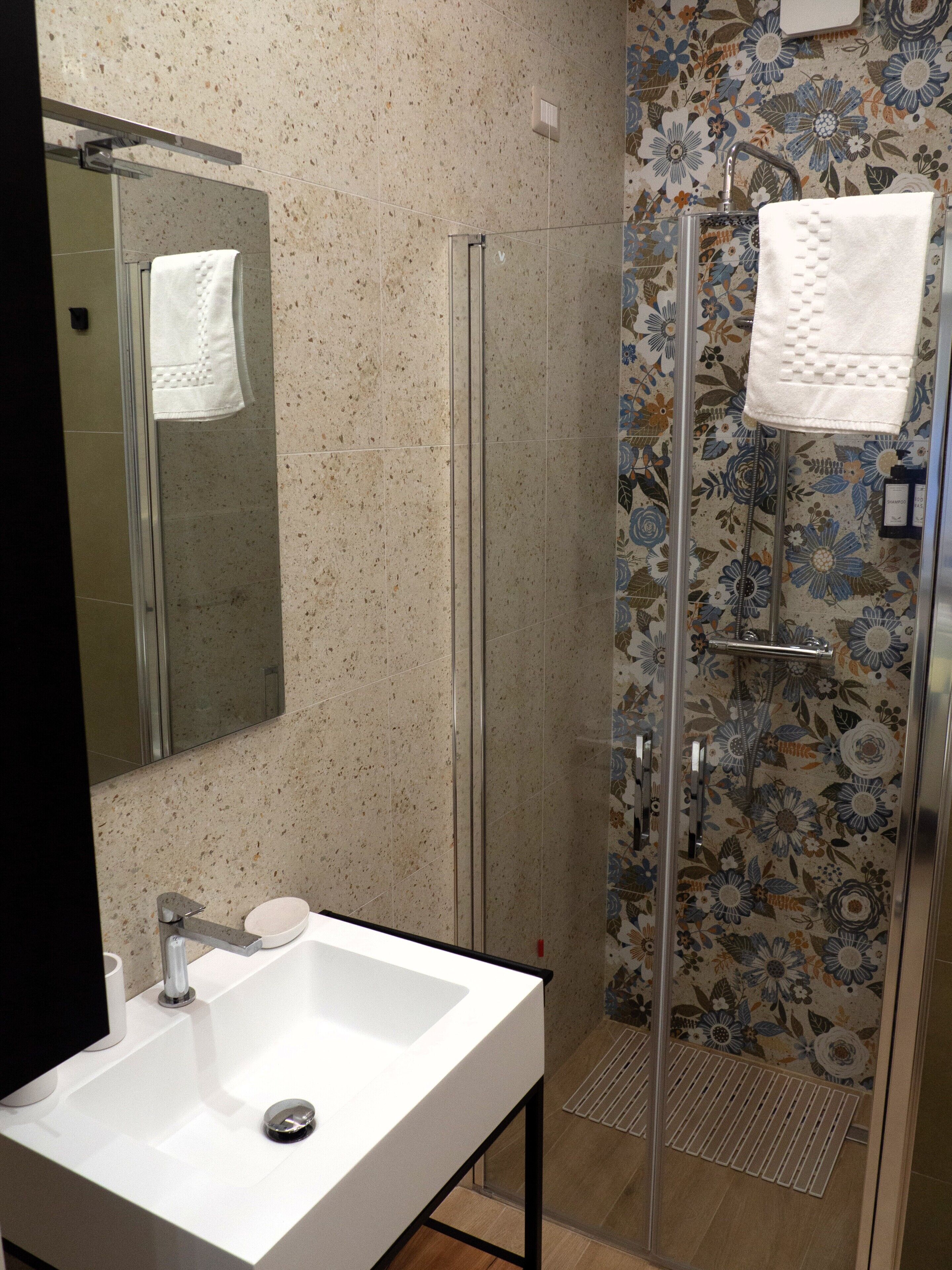 A bathroom with a glass shower enclosure, a white sink, and a mirror.
