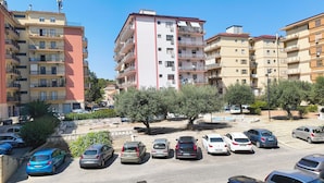 Un aparcamiento con varios coches, rodeado de edificios residenciales de varios pisos con balcones y aires acondicionados.