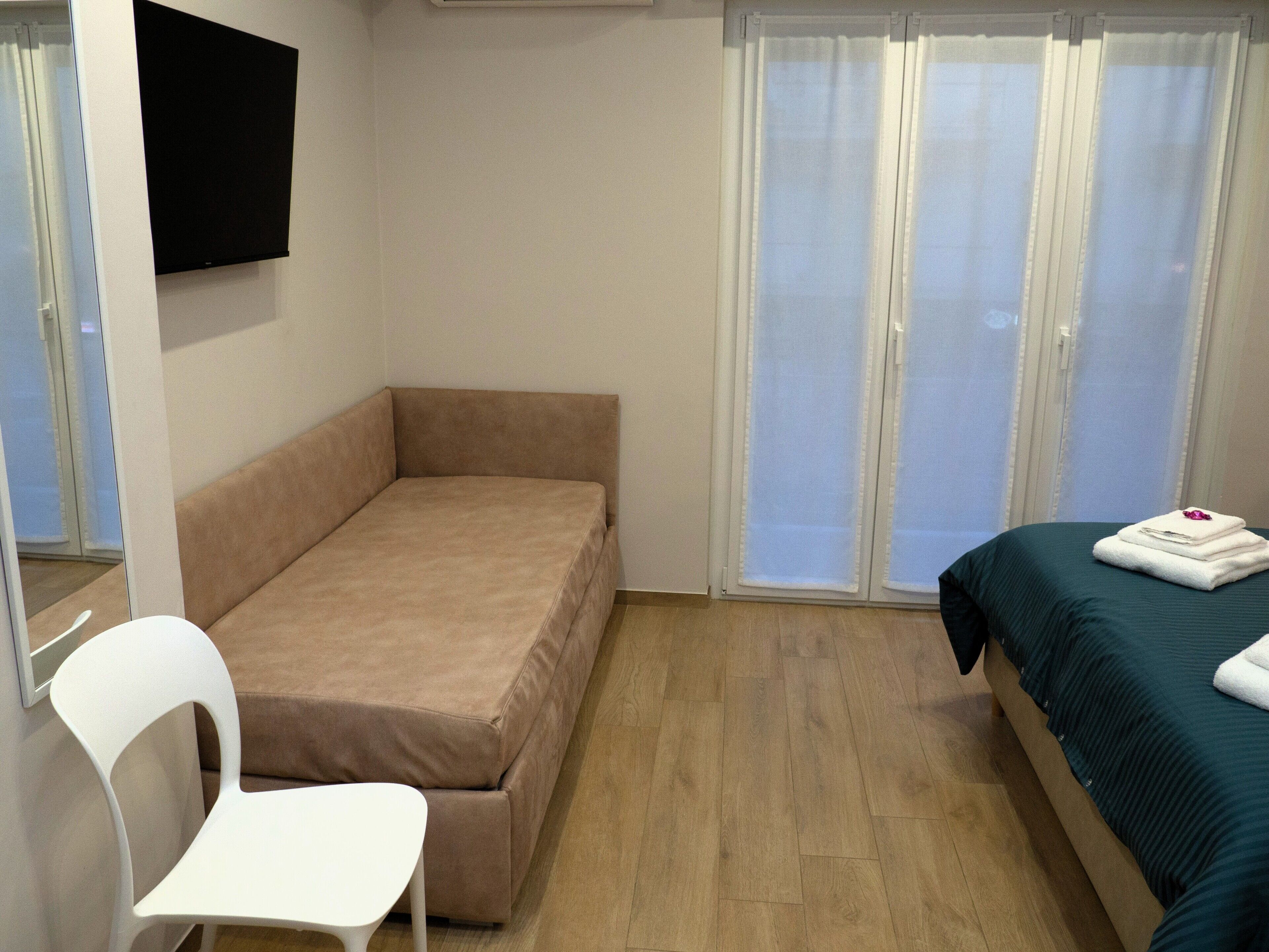 Un alojamiento pequeño y de una sola habitación, con cama, una silla y televisor montado en la pared.