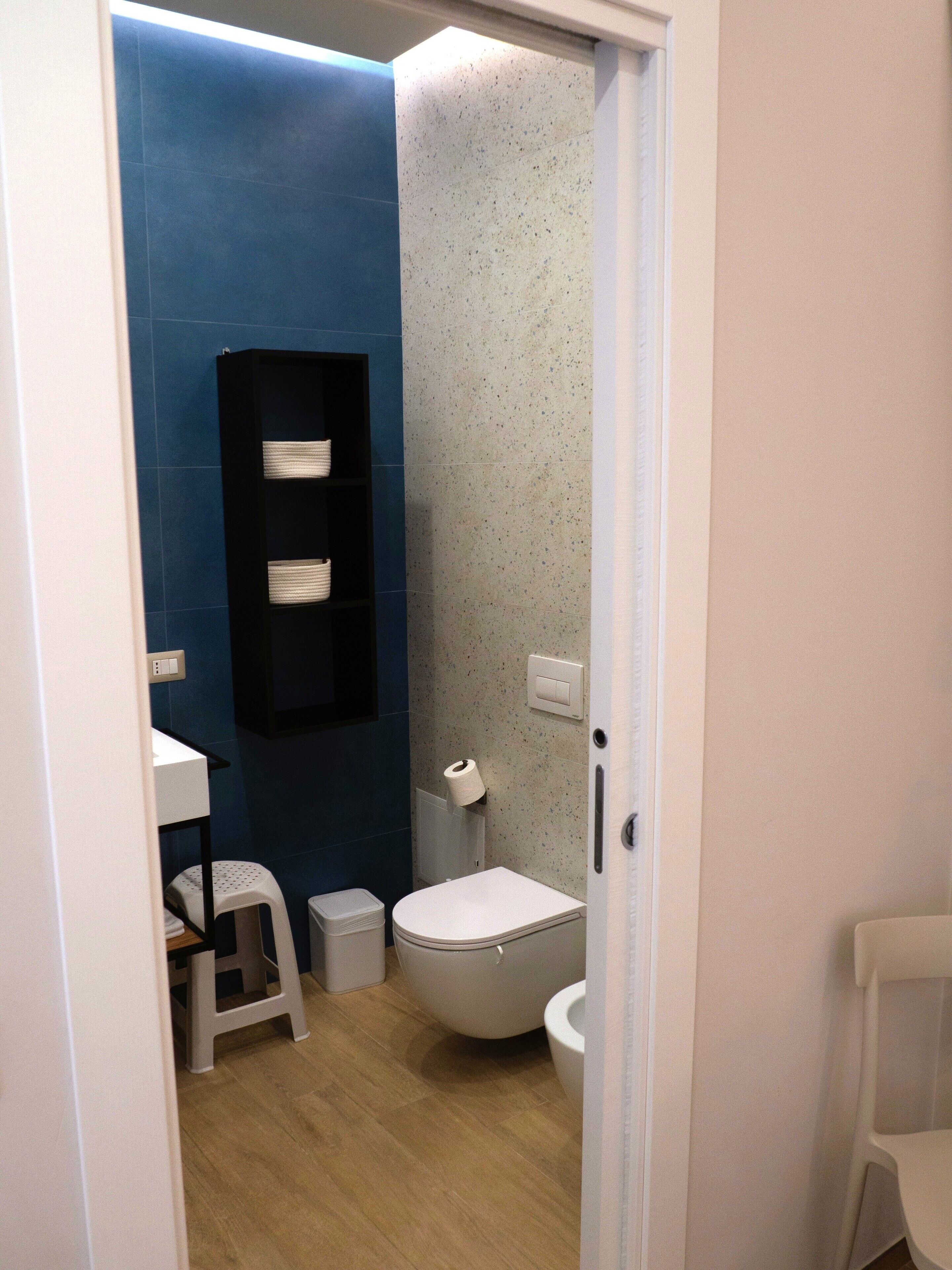 A compact bathroom with a toilet, a small sink, and a shelf with towels.