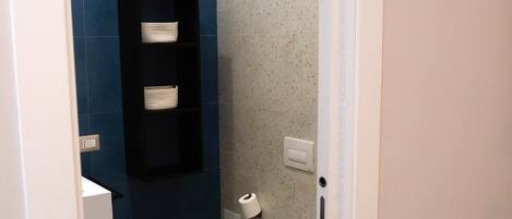 A compact bathroom with a toilet, a small sink, and a shelf with towels.