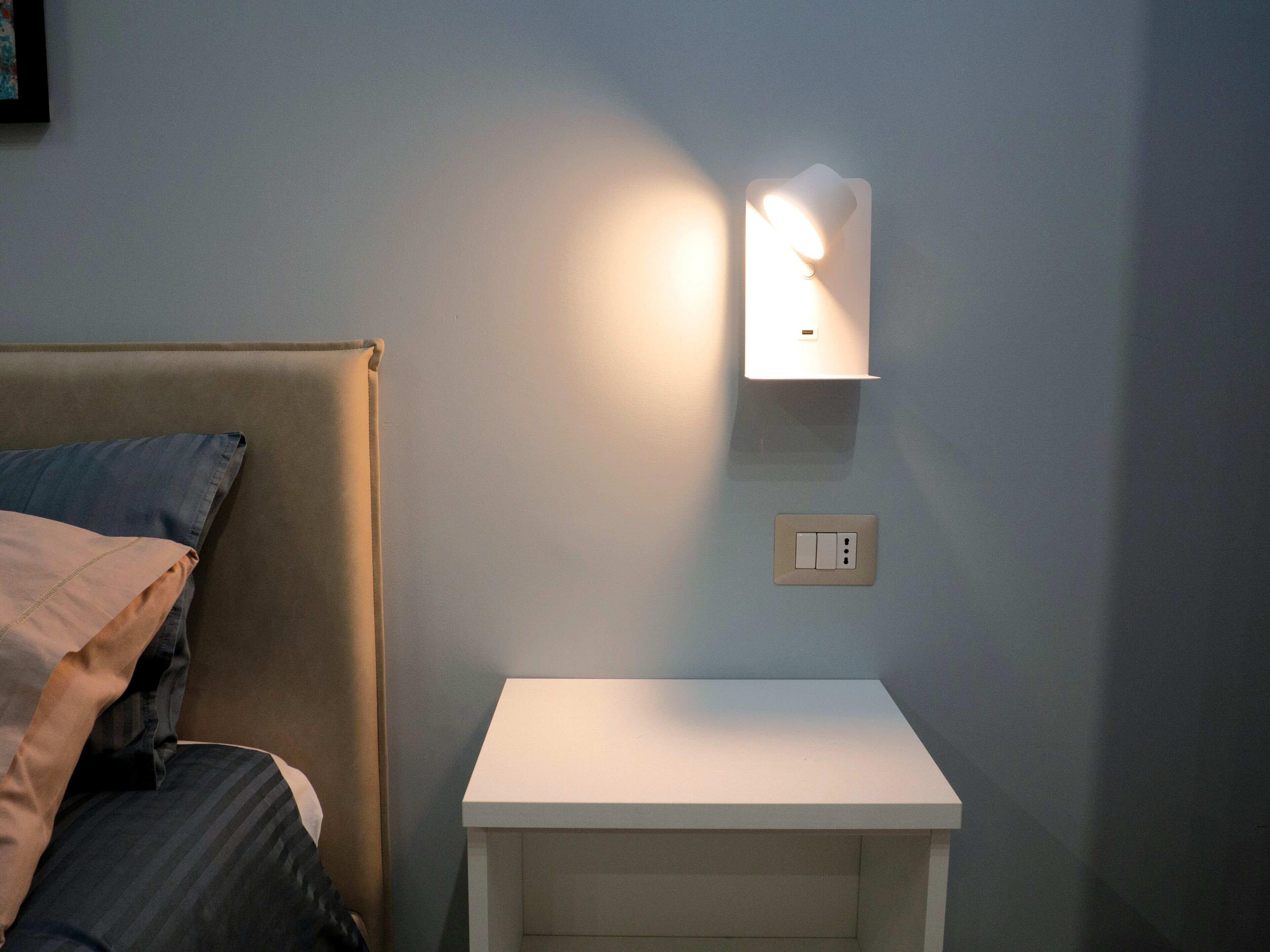 Une chambre à coucher avec un lit, une table de chevet et un luminaire fixé au mur.