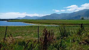 A serene landscape with a lake, green fields, and mountains in the background. - Tannenhof Guest Farm (Tsitsikamma)