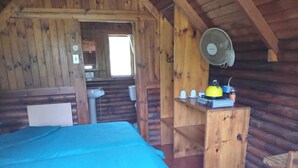 A cozy cabin room with a bed, a small table with a kettle, cups, and a fan. - Tannenhof Guest Farm (Tsitsikamma)