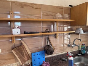 A kitchen with wooden shelves holding kitchenware, a sink with a faucet, and a blue cleaning tool on the counter. - A clean and sunny apartment in the heart of Siwa (Siwa Oasis)