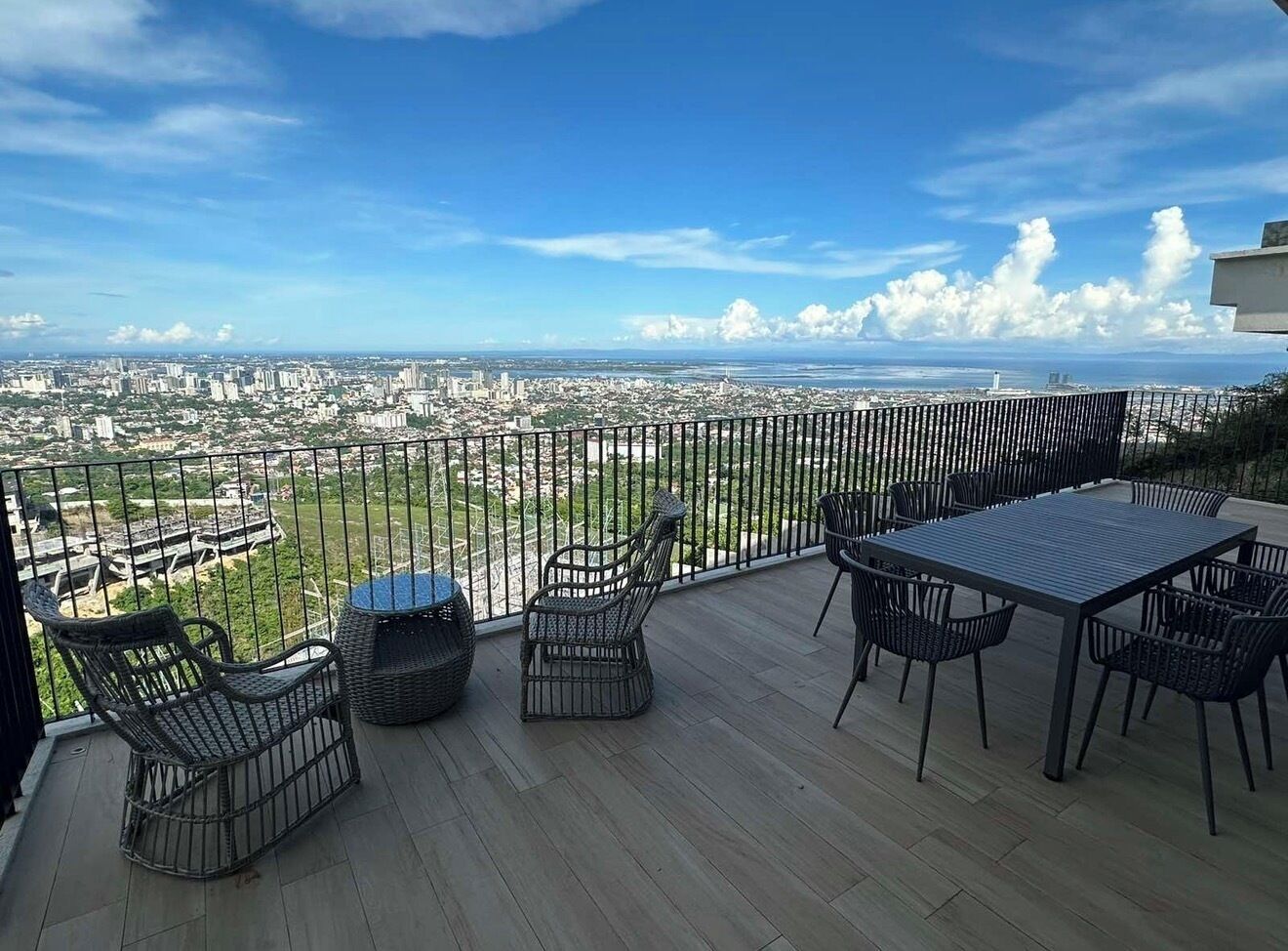 A balcony with a view of a cityscape, furnished with wicker chairs and a table.