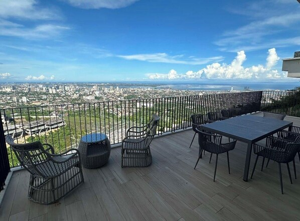 A balcony with a view of a cityscape, furnished with wicker chairs and a table.