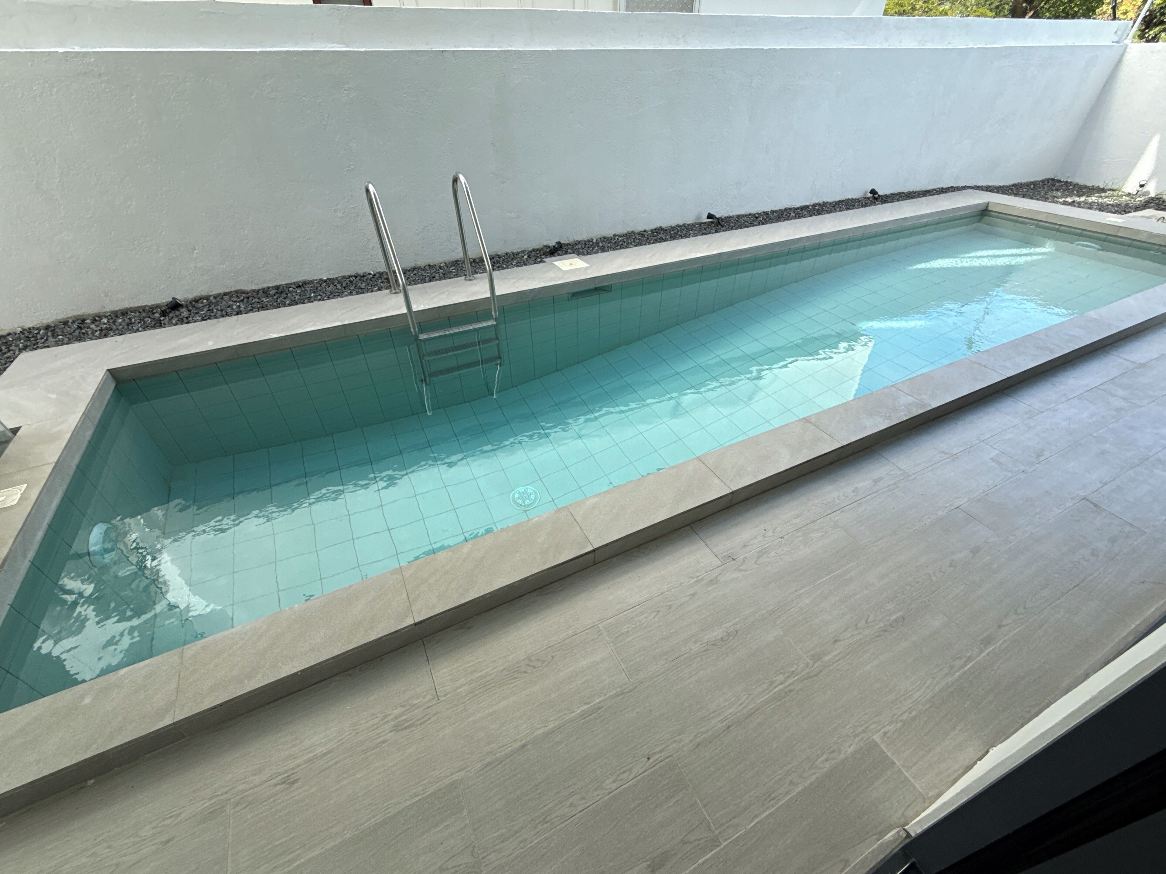 A rectangular swimming pool with a tiled interior and a wooden deck surrounding it.