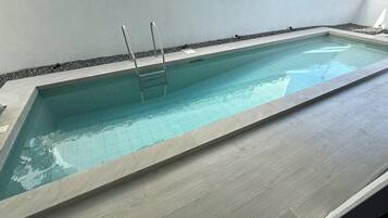 A rectangular swimming pool with a tiled interior and a wooden deck surrounding it.