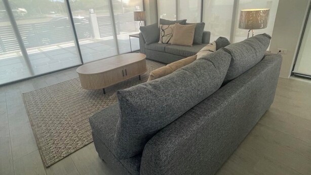 A spacious living room with a grey sofa, a coffee table, and a lamp. Large windows provide a view of the outside. - Spacious 4-bedroom house in wonderful San Juan with AC close to beachfront (San Juan)