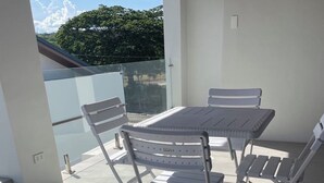 A sunlit outdoor patio with a metal table and chairs, a glass balustrade, and a view of greenery. - Spacious 4-bedroom house in wonderful San Juan with AC close to beachfront (San Juan)