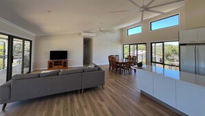 A spacious living area with a grey sofa, wooden dining table, and ceiling fans.