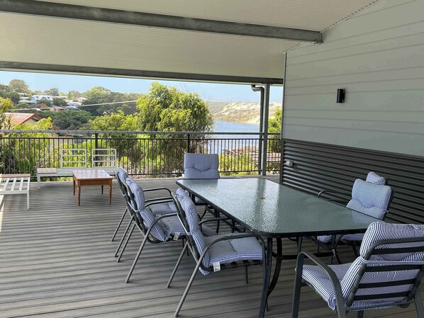Un patio techado al aire libre con una mesa y sillas, vistas a un cuerpo de agua y una barandilla.