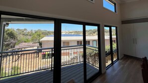 A room with large windows, a balcony, and a view of a residential area.